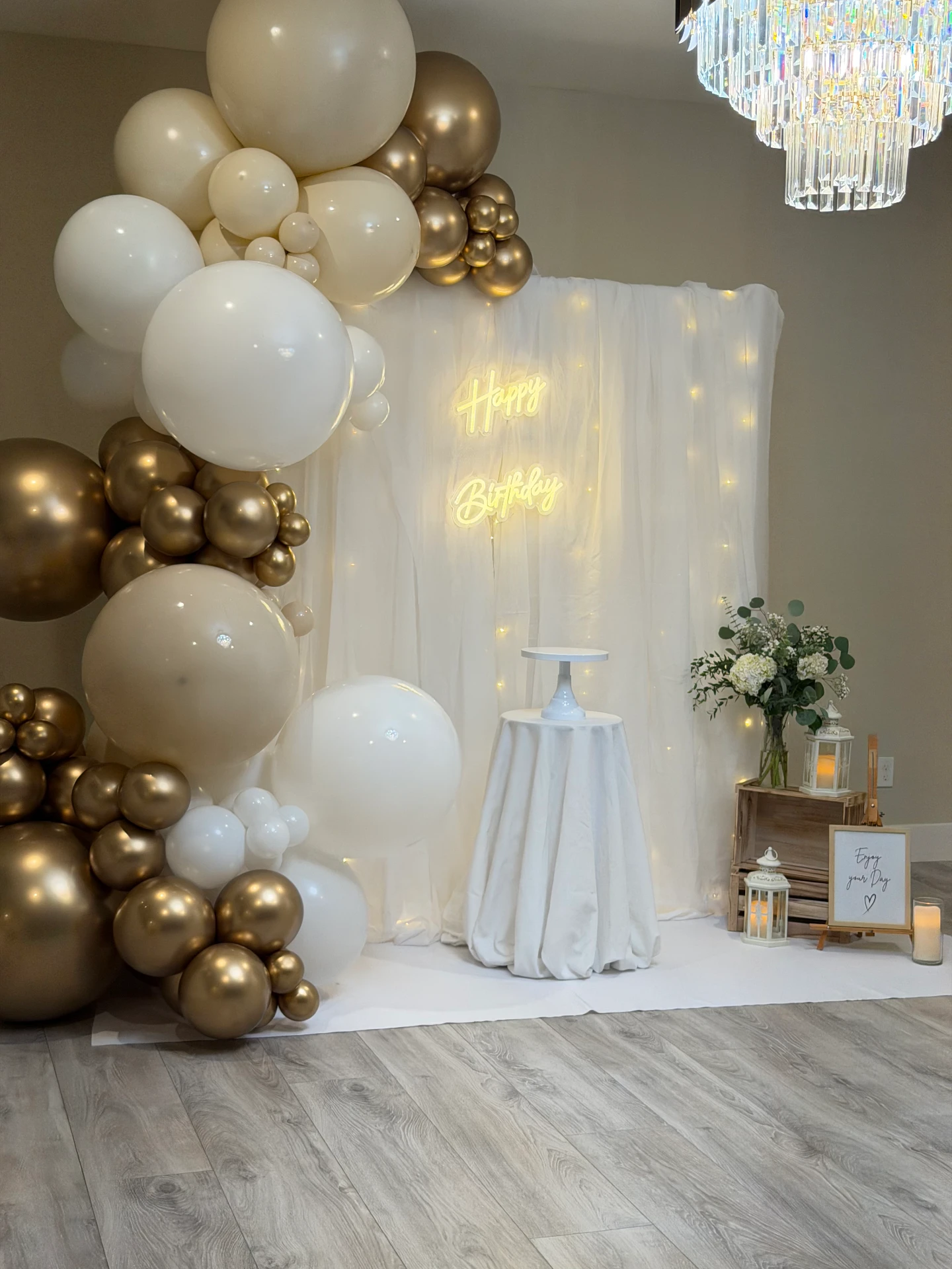 Elegant white and gold birthday balloon installation with a draped light backdrop